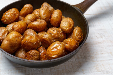 roasted potatoes in a frying pan, whole cooked food, delicious crust, one object on a white wooden boards background