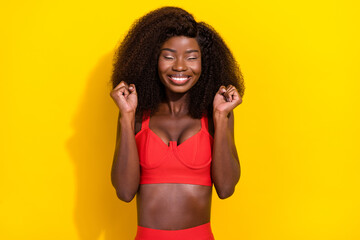 Photo of lucky funny afro girl wear red sexy outfit rising fists closed eyes smiling isolated yellow color background