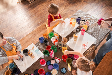 Kids listening their teacher while standing at the table full of paints and preparing to the drawing