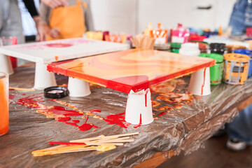 Two abstract paintings drying at the plastic cups. Kids and teacher at the background