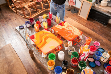 Woman standing in front of the table with a lot of paints and looking at her two abstract drawings