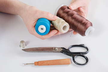 Woman holds spools of thread of different colors in her hands. There are scissors and a seam ripper on the table. Seamstress workplace, tools for sewing and repair clothes.