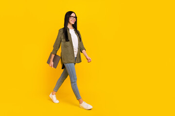 Full size photo of cute young lady hold laptop go wear spectacles shirt jeans footwear isolated on yellow background