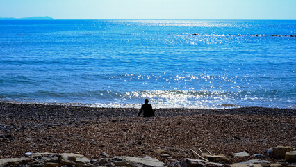 man sitting on an empty beach looks at the blue sea. "Pioppi", Campania. Italy
