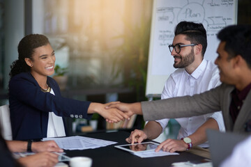Building business relationships. Shot of two businesspeople shaking hands together in a boardroom while colleagues look on.