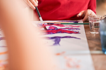 Cropped view of the little kid drawing with acrylic paints at the paper