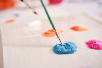 Cropped view of the kid taking glitter on the brush while decorating his painting at the art school