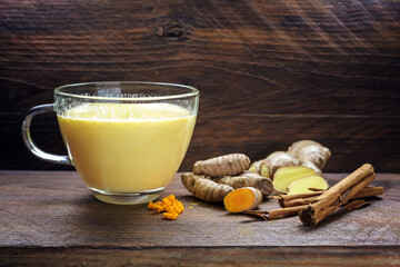 Golden milk from turmeric, ginger, cinnamon and other spices, healthy ayurvedic drink and trendy natural detox beverage on dark rustic wooden planks, copy space, selected focus