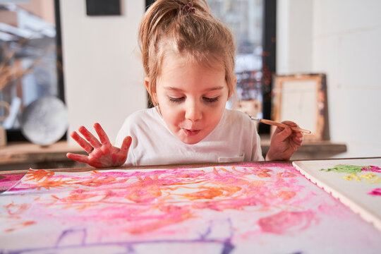 Caucasian child girl blowing at the picture with glitter while creating at the art school