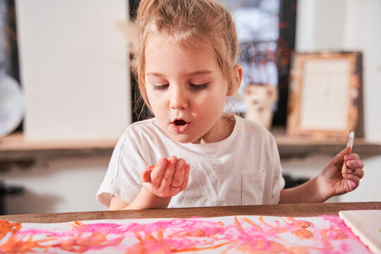 Caucasian child girl blowing at the glitter at her hand while creating picture