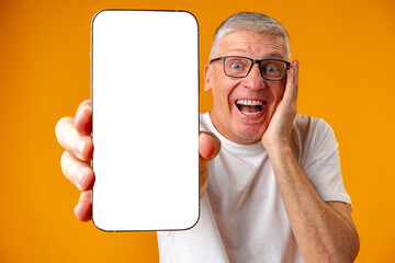 Photo of senior surprised man point finger at smartphone over yellow background