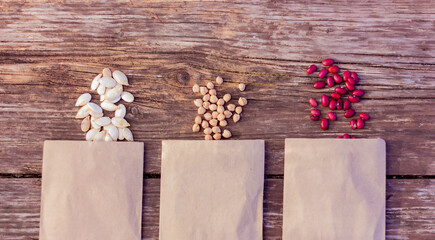 bean, chickpea and pumpkin seeds in paper bags on a rustic wooden table, close-up top view. concept of farming, gardening, planting organic natural products.