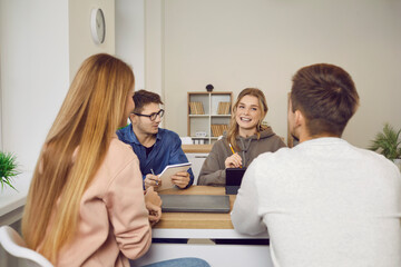 Smiling diverse multiethnic students sit at desk work study together with electronic gadgets. Happy young people learning preparing for test or exam for university or college. Education concept.