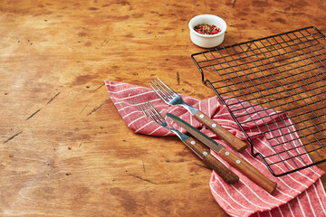 Forks, knife, napkin, empty baking rack and peppercorns in small bowl on wooden background