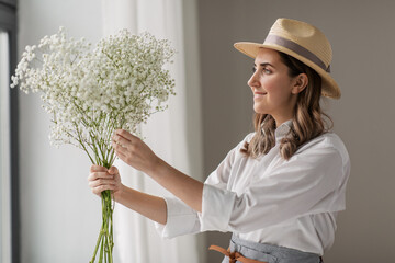 people, gardening and floral design concept - happy smiling woman or floral artist in straw hat...