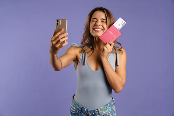 Young white woman taking selfie photo while holding passport with tickets - obrazy, fototapety, plakaty