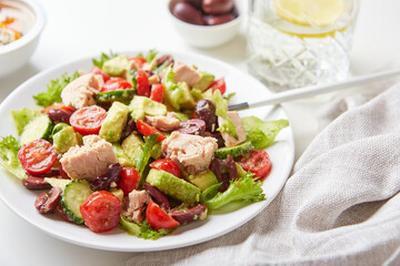 Salad with tuna, lettuce, cucumbers, tomatoes, olives and avocados in white plate on the table