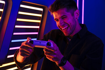 Young bristle man laughing while playing video game with joystick