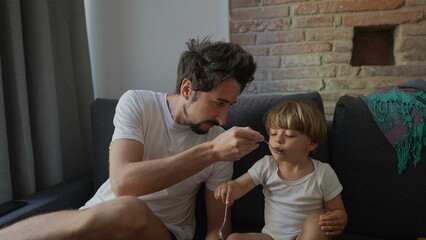Fototapeta premium Candid family moment father feeds toddler child yogurt breakfast in morning