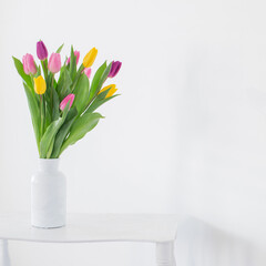 tulips in white vase on wooden shelf on white background