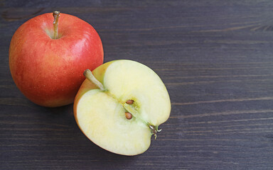Fresh ripe half cut red apple with a whole fruit on black wooden table