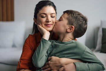 Mother's day, caring young son, kissing his mother's cheek, while she enjoys. - obrazy, fototapety, plakaty