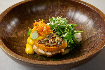 Pumpkin steak with chicken and spinach on dark ceramic plate. Healthy food in modern dishware. Innovative recipes in contemporary style. Roasted turkey with pumpkin on gray concrete background.