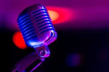 Fototapeta na wymiar Classic stage microphone. Object illuminated with colored light. In the background, a view of blurred lights on the stage.