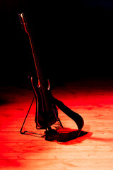 Fototapeta na wymiar A black electric guitar based on a stand placed on the stage. Subject illuminated by strong red light.