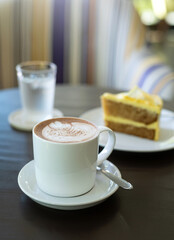 cup of hot coffee art with cake on wooden table in cafe