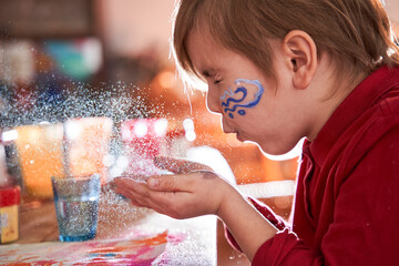 Cute child boy holding glitter at his hand and blowing on it with closed eyes while creating