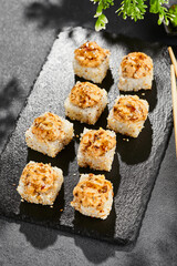 Baked Maki sushi on dark slate. Hot unagi maki with eel. Sushi roll with baked eel, cheese and unagi sauce topped. Style concept japanese menu with black background, leaves and hard shadow.