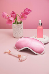 gentle background for cosmetics product presentation with rose quartz massage roller, sleeping mask and  bottle of cosmetic oil or serum. Mock up of skin care at home