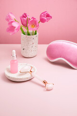 gentle background for cosmetics product presentation with rose quartz massage roller, sleeping mask and  bottle of cosmetic oil or serum. Mock up of skin care at home