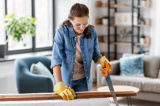 Repair, Diy And Home Improvement Concept - Happy Smiling Woman In Goggles With Saw Sawing Wooden Board