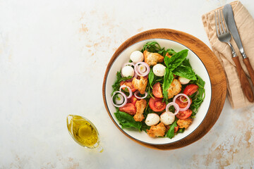 Panzanella Bread Salad. Traditional food of Italy with tomatoes, mozzarella balls, basil, onion and bread on plate on light background. Traditional Italian cooking. Top view. Copy space.