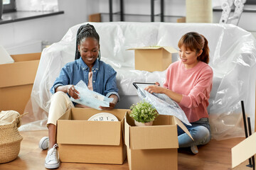 moving, people and real estate concept - women unpacking boxes at new home or packing stuff into...