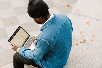 Black young man working with laptop while sitting on bench