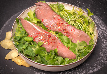 Raw pork tenderloin, sirloin and fresh herbs on a plate, on black background. Cooking concept with raw meat.