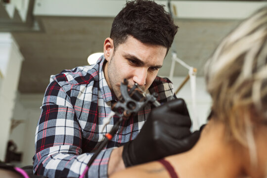 young tattooist man tattooing a woman's back