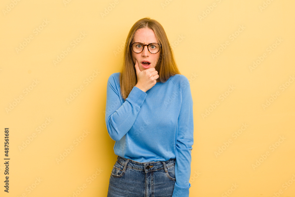 Wall mural pretty caucasian woman with mouth and eyes wide open and hand on chin, feeling unpleasantly shocked, saying what or wow