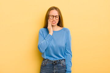 pretty caucasian woman holding cheek and suffering painful toothache, feeling ill, miserable and...