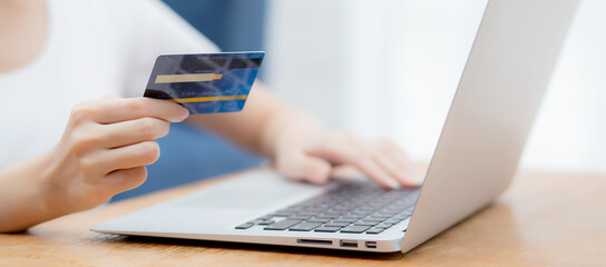 Hand of young woman holding credit card buying shopping online with laptop computer, girl purchase...