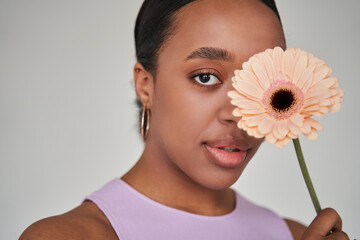 Brunette multiracial woman closed one eye with the flower while looking at the camera