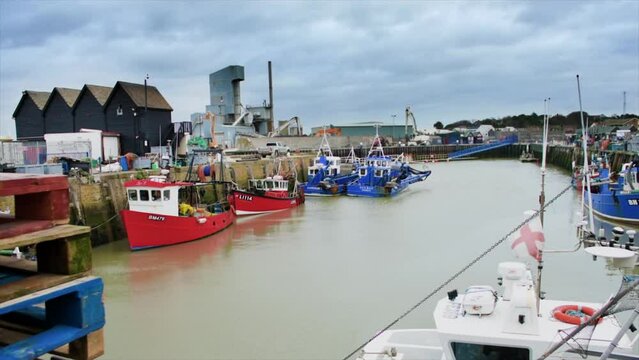 A small and quintessentially English wharf in the seaside town of Whitstable in the Shire of Kent, with pallets, trawlers and other small boats