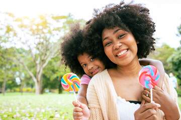 Beautiful mom and her daughter holding Multi-Colored Rainbow Hard Lollipop Candy while picnic at the park. Concept of relaxing and special holiday