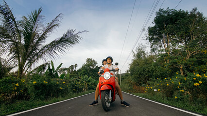 Love couple on red motorbike in white clothes to go on forest road trail trip. Two caucasian tourist woman man drive on scooter. Motorcycle rent, safety helmet, sunglasses. Asia Thailand ride tourism.