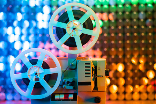 Retro reel with film rotating on colorful shining sparkles wall