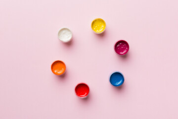 jars with gouache of different colors on Colored background. hobby painting. Top view with empty...