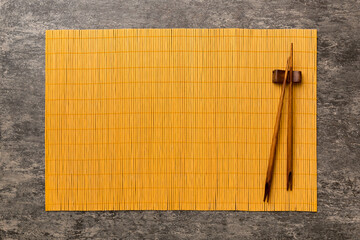 Two chopsticks and bamboo mat on cement background. Top view, copy space